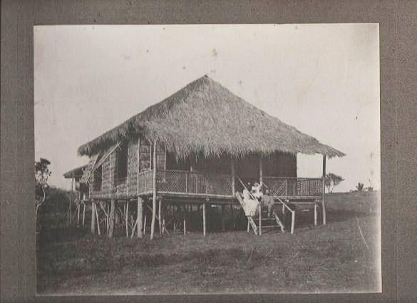 Item #037412 VINTAGE PHOTOGRAPH OF A PHILIPPINO SOLDIER IN UNIFORM (SPANISH-AMERICAN WAR), POSED WITH A WOMAN AND A CHILD ON THE STEPS OF A NIPA HUT. Philippine Islands.